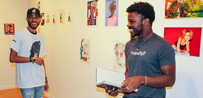 2 BSU students st和 in front of their exhibits smiling in the Wallace Anderson Art Gallery on campus